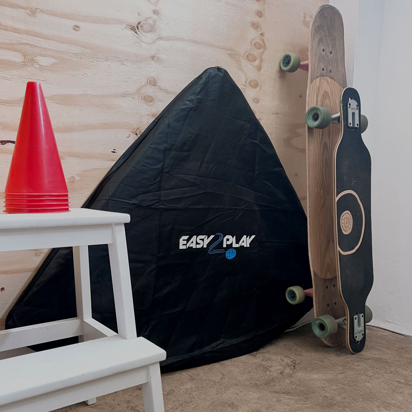 Ein Easy2Play Fussballtor Set steht an die Wand gelehnt, daneben zwei Longboards und ein Hocker
