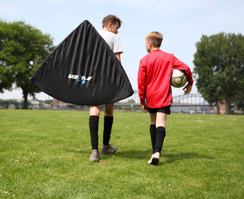 Zwei Jungen gehen über die Wiese, der linke Junge trägt ein Easy2Play Tor über der Schulter in einer Tragetasche